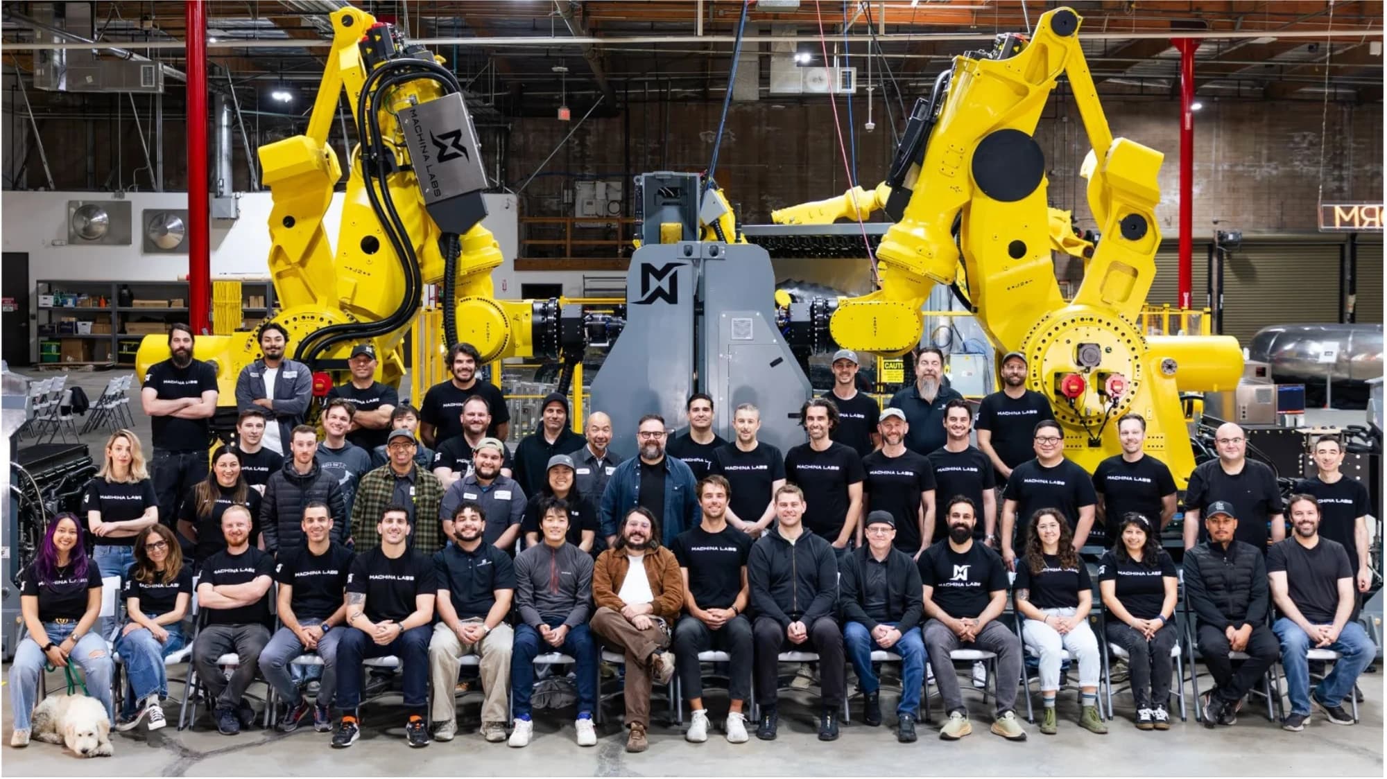 Equipo de trabajo reunido frente a los robots y la maquinaria del taller